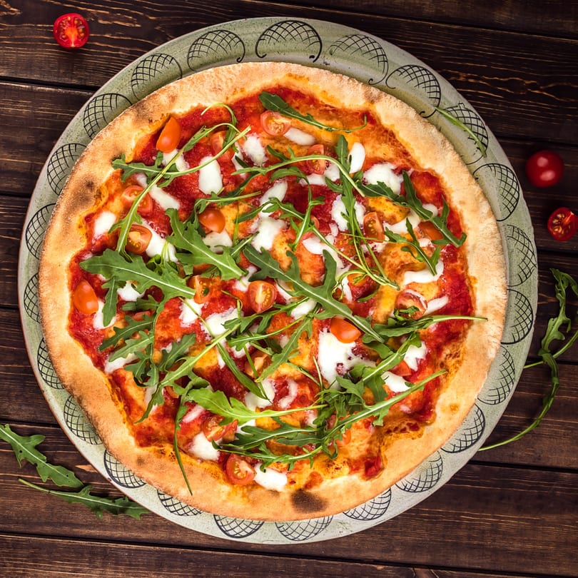 Pizza Heaven's pizza with tomato sauce, mozzarella, cherry tomatoes, and arugula on a rustic wooden table.