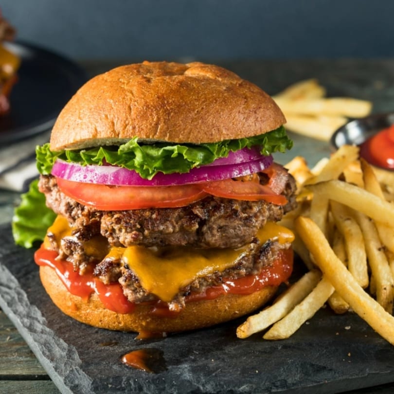 A double cheeseburger with lettuce, tomato, onion, and ketchup, served with french fries.