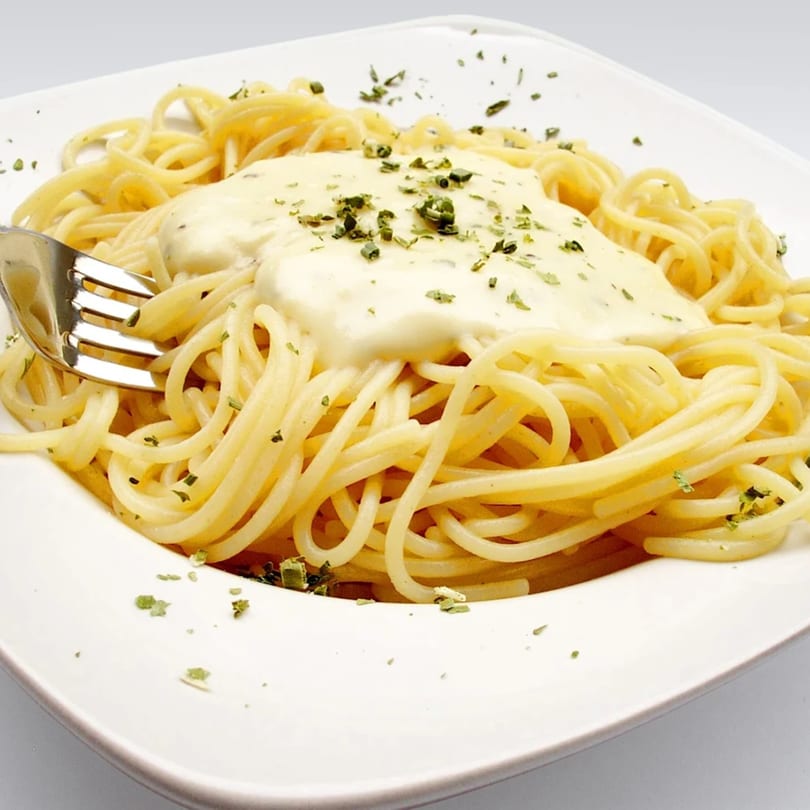 Spaghetti with creamy white sauce and green herbs on a white plate, with a fork.