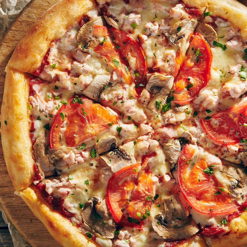 Close-up of a Pizza Heaven pizza with tomatoes, mushrooms, chicken, and melted cheese.