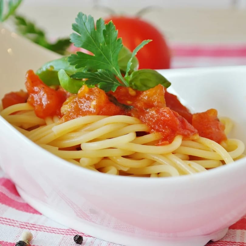 Spaghetti with chunky tomato sauce, fresh basil, and parsley in a white bowl.