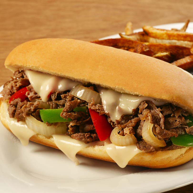 A cheesesteak sandwich with steak, onions, peppers, and melted cheese, served with fries.